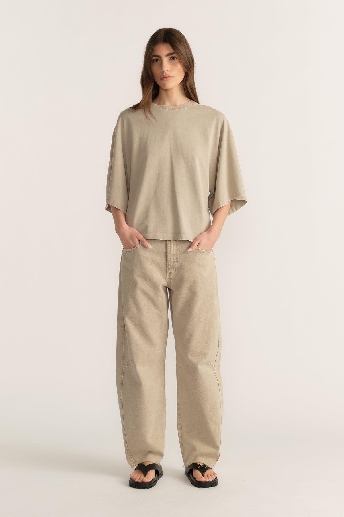 Woman wearing a beige oversized tee with relaxed barrel-leg jeans and black sandals