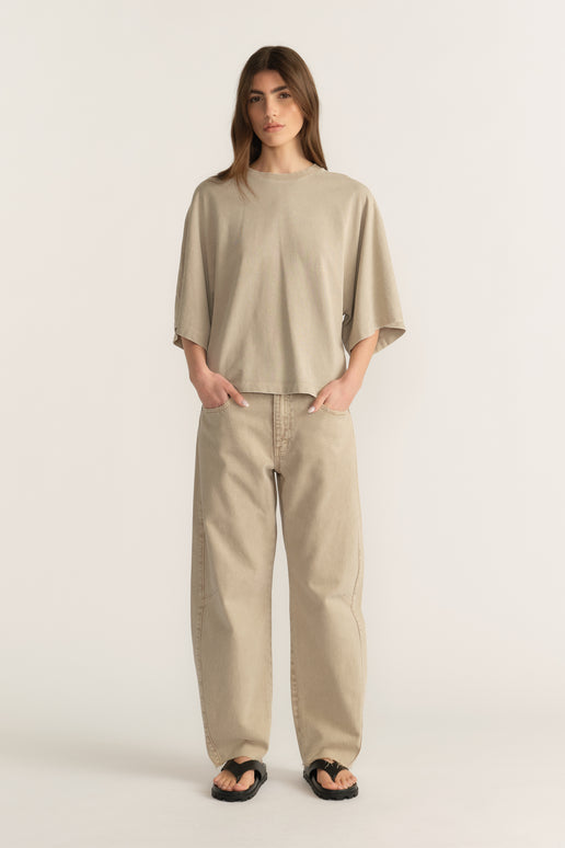 Woman wearing a beige oversized tee with relaxed barrel-leg jeans and black sandals