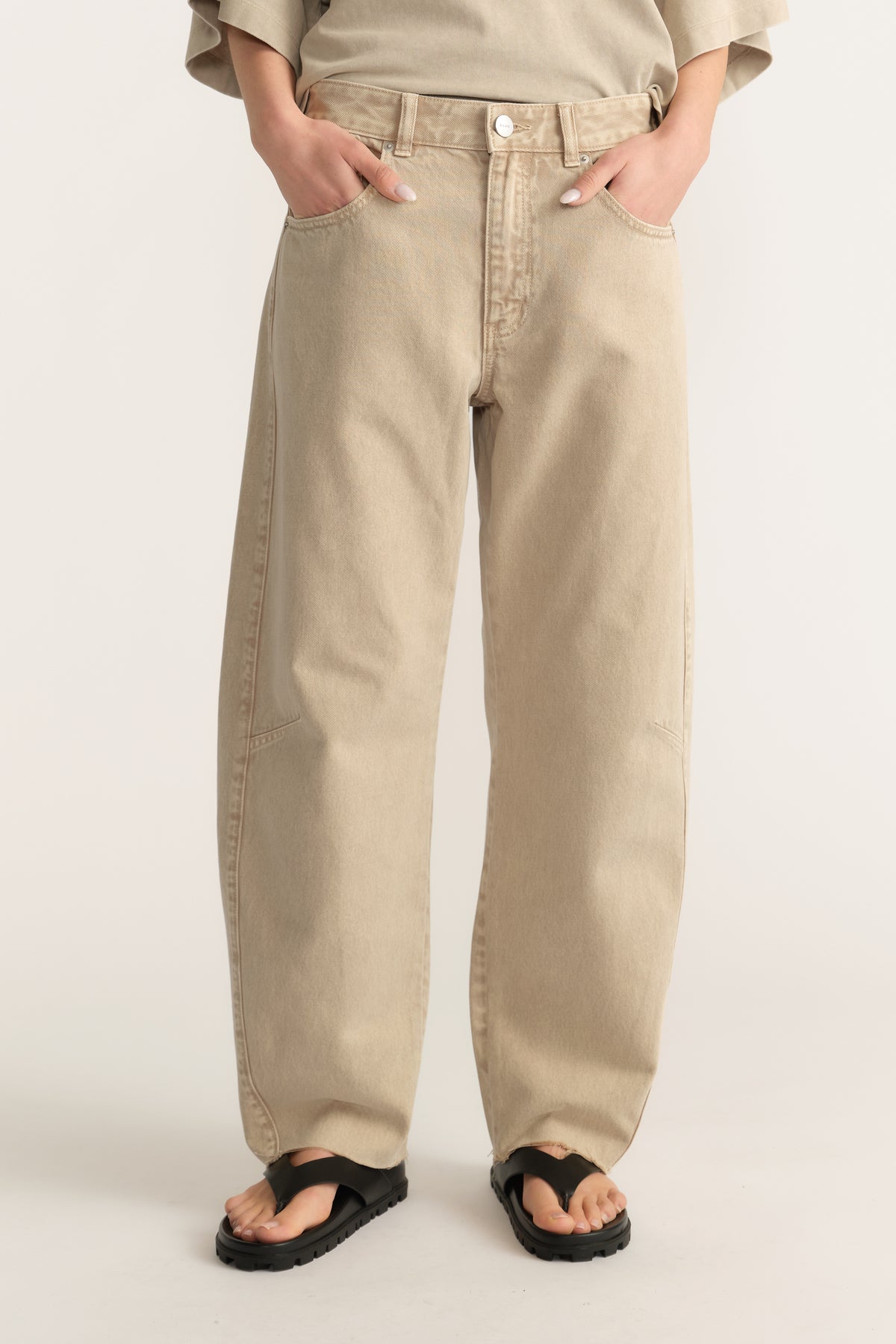Woman wearing beige barrel leg jeans with a mid waist, curved relaxed fit and raw edge hems
