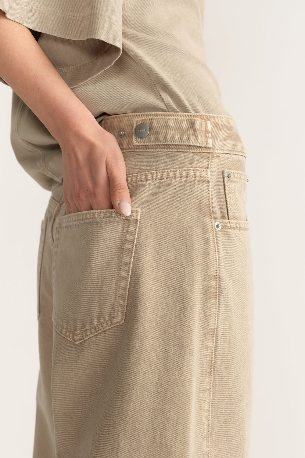 Woman wearing stone beige barrel leg jeans with an adjustable waistband and back pockets