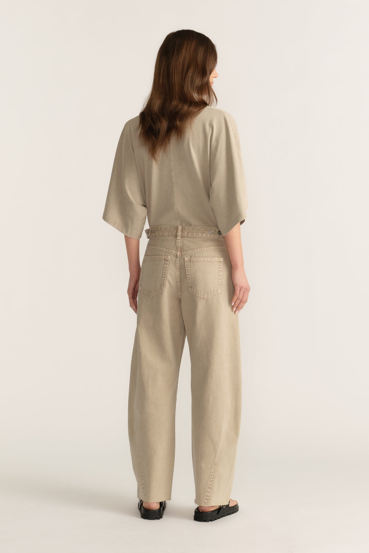 Back view of woman wearing beige barrel leg jeans with a cinched waistband and relaxed ankle length fit