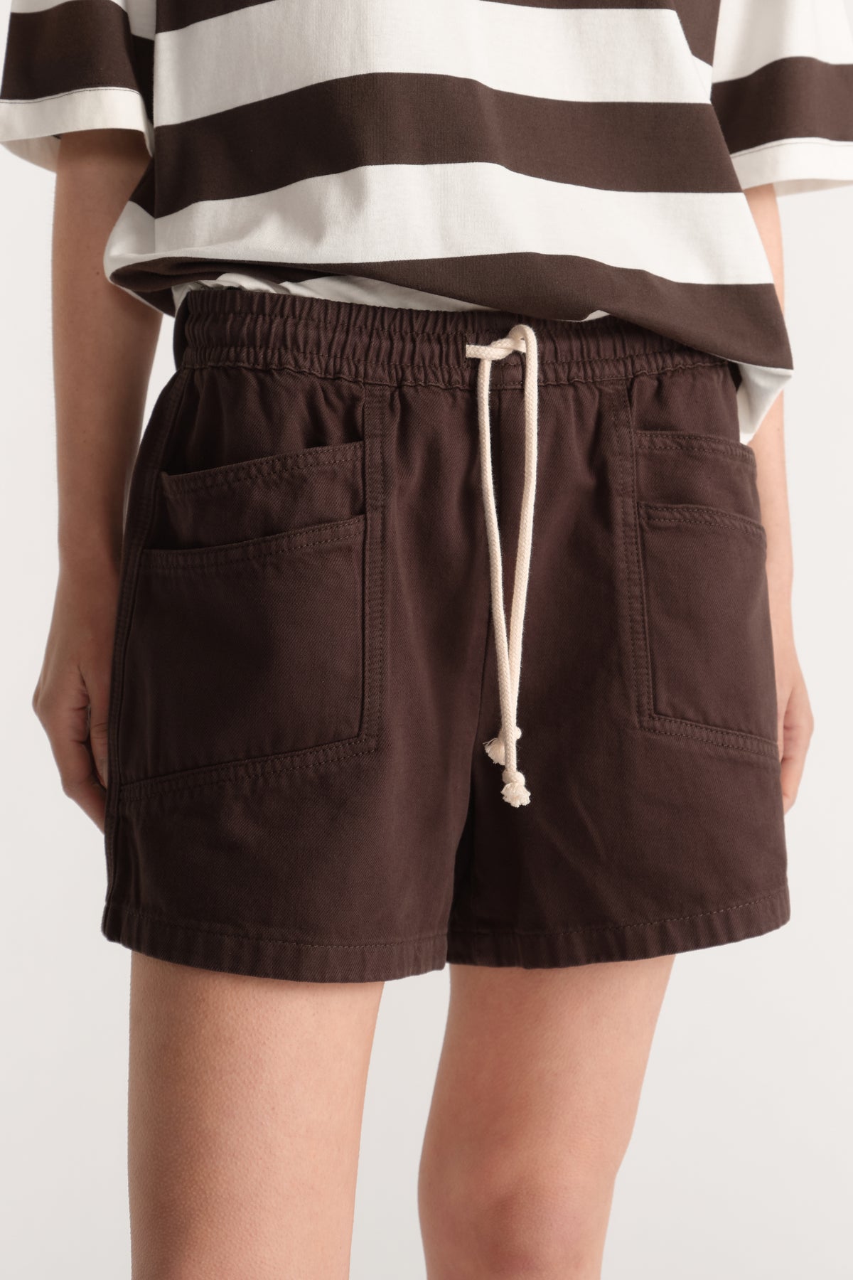 Model wearing dark brown denim shorts with an elastic waist, white drawstring and patch pockets