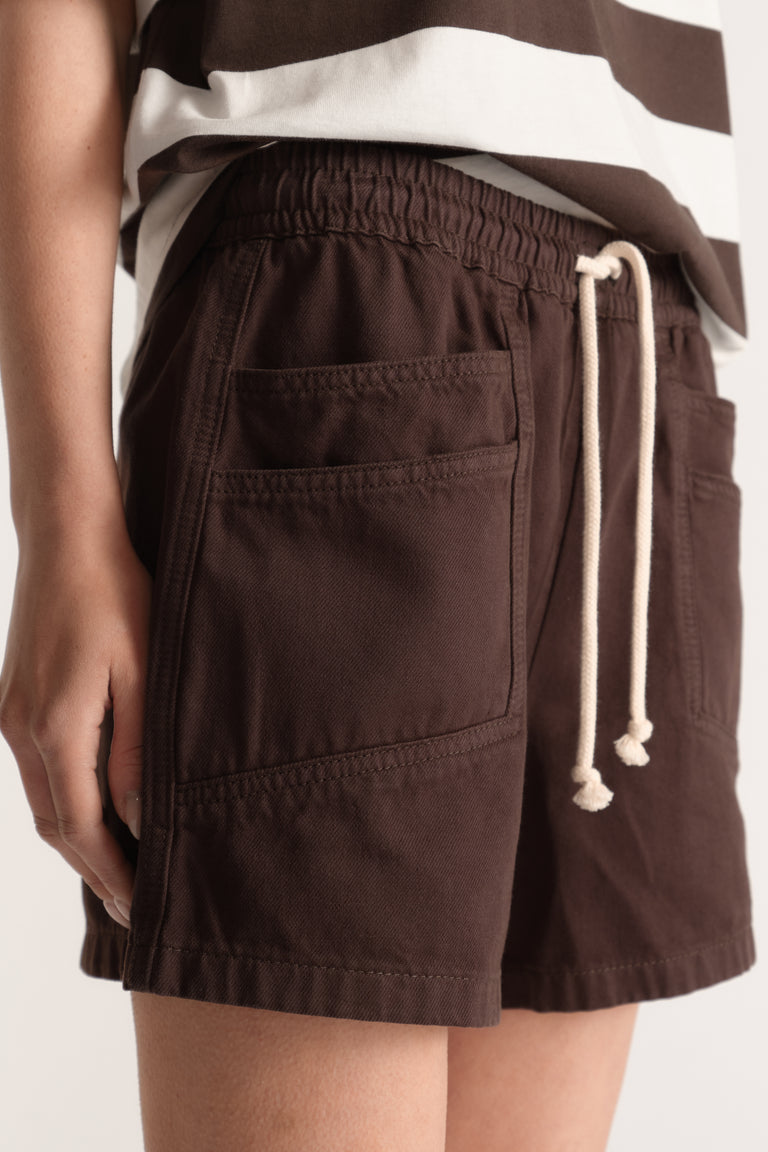 Woman wearing dark brown denim shorts with an elastic waist, drawstring tie and utility pockets