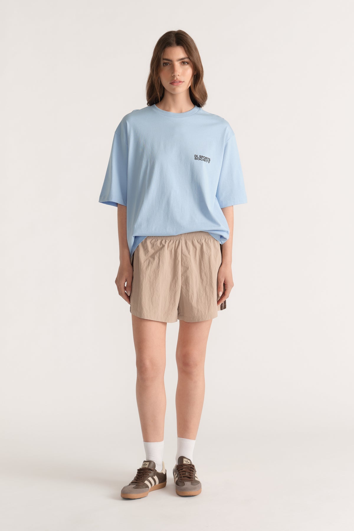 Woman wearing a relaxed light blue tee with beige drawstring shorts and brown sneakers