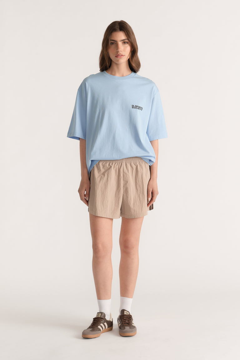 Woman wearing a relaxed light blue tee with beige drawstring shorts and brown sneakers