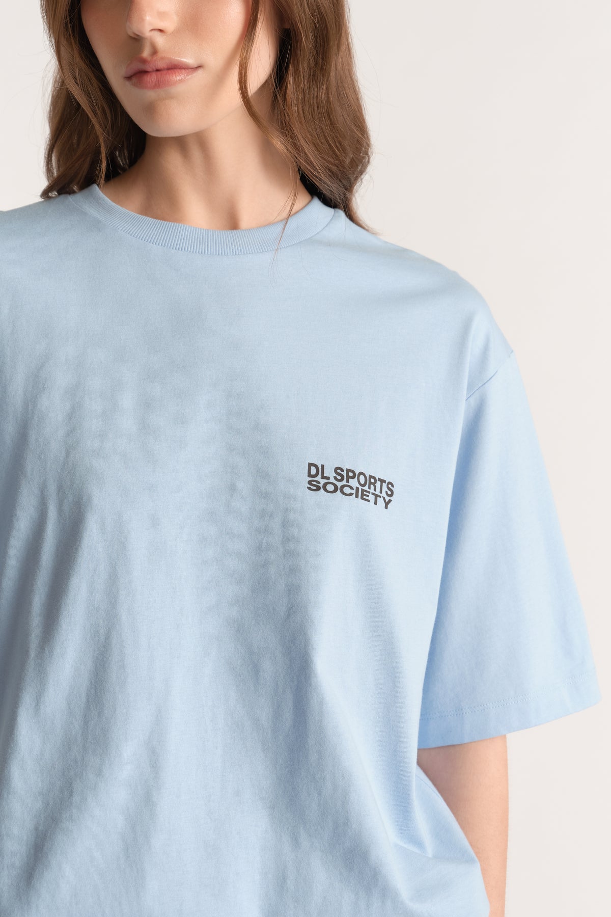 Woman wearing a light blue relaxed fit tee with a small sports society chest logo