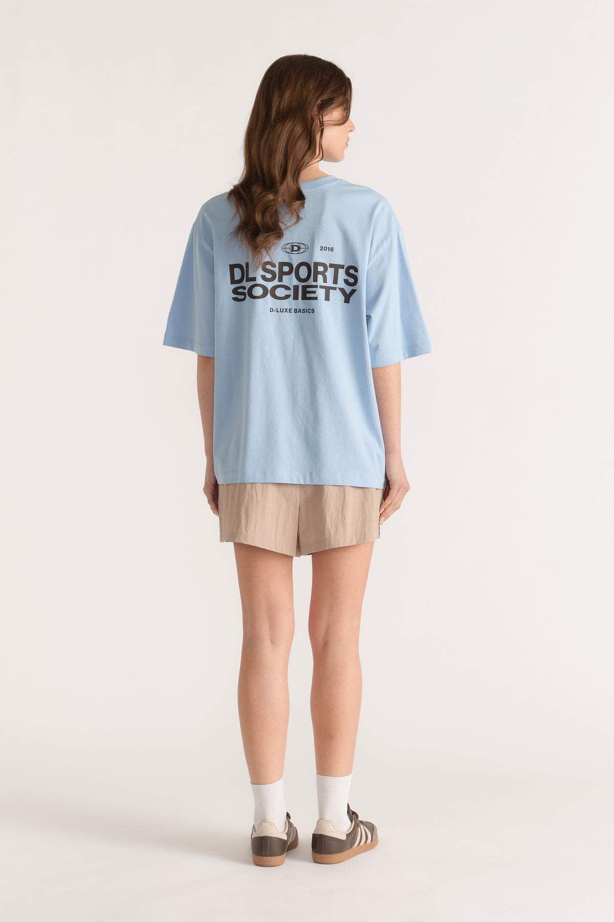 Back view of model wearing a light blue D Luxe sports graphic tee with beige shorts and sneakers
