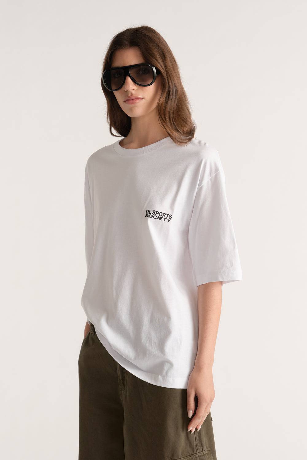 Woman wearing a white relaxed fit graphic tee with olive trousers and oversized black sunglasses