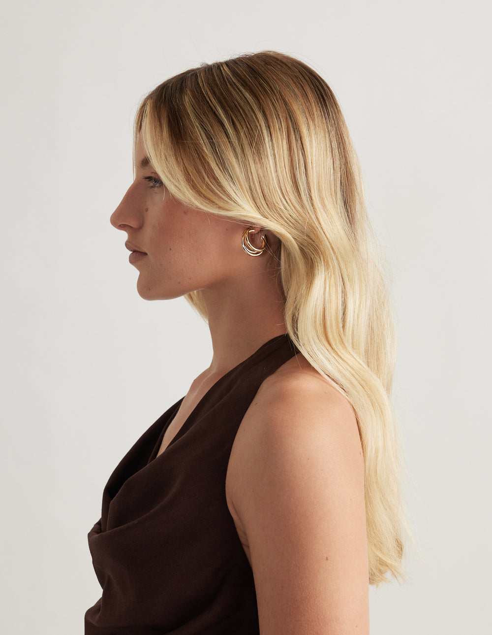 Woman in profile wearing a small polished gold hoop earring against a neutral background