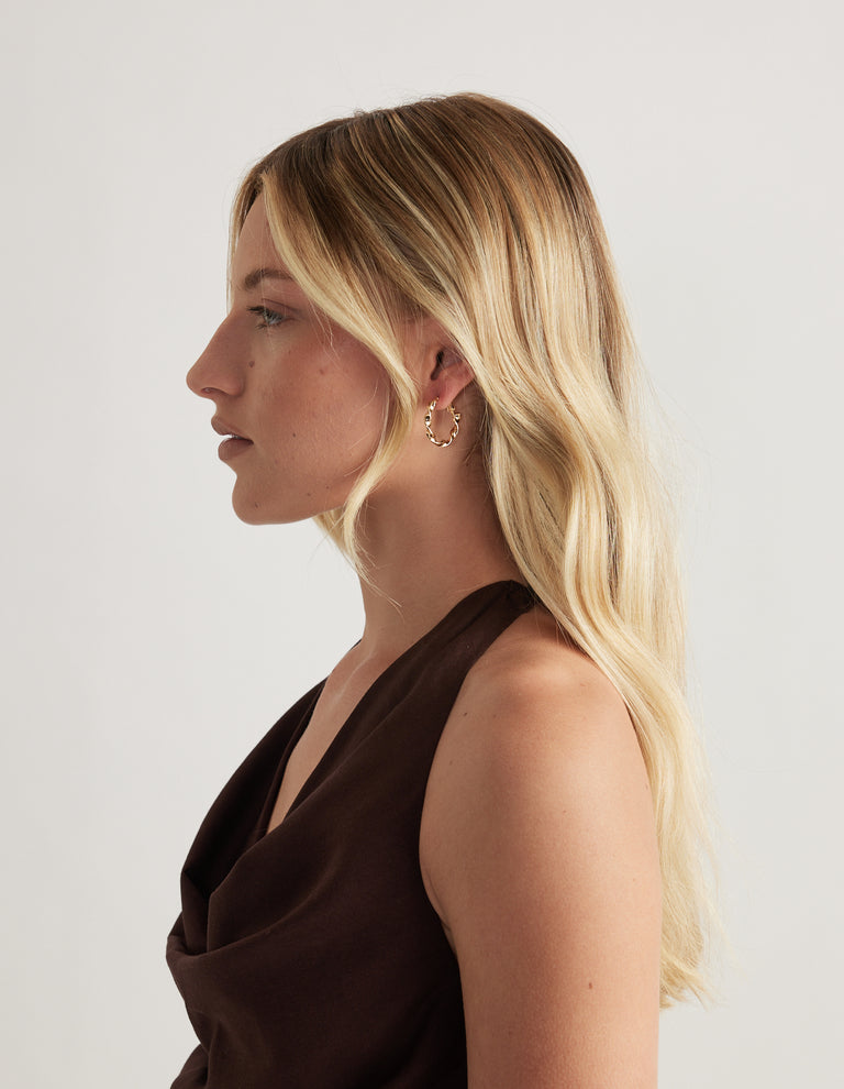 Woman in profile wearing a small shiny gold hoop earring with a dark brown sleeveless top