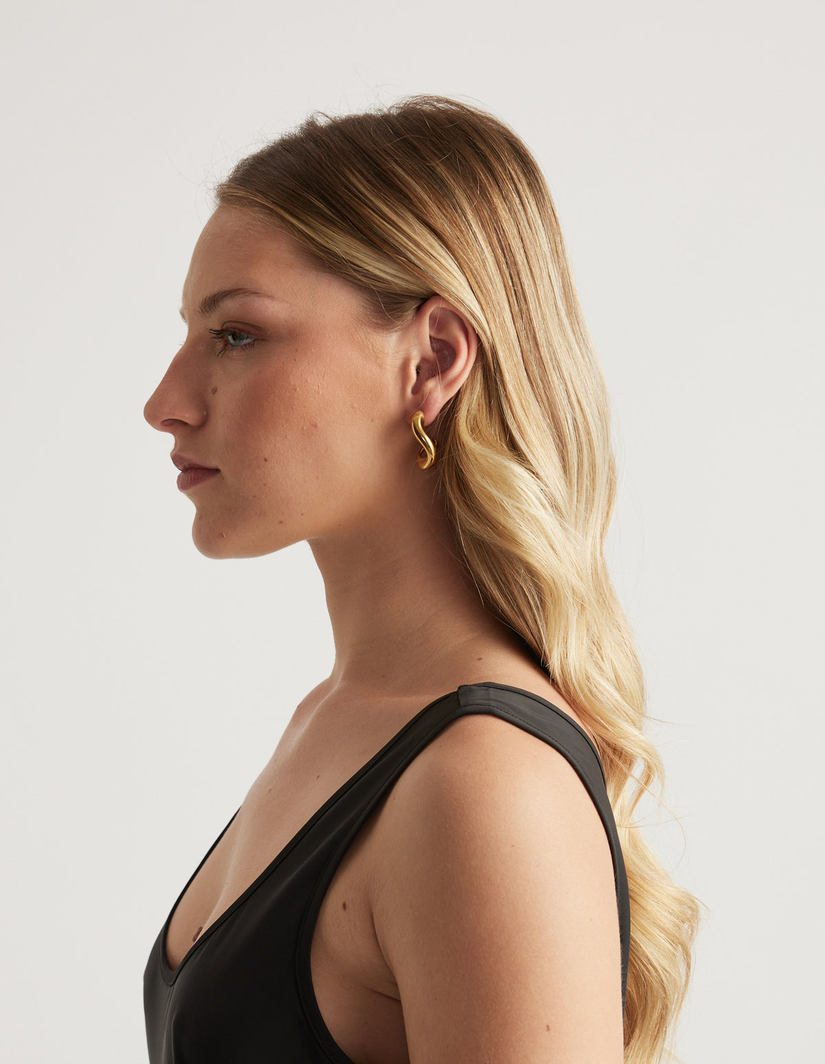 Woman in profile wearing a gold wavy hoop earring and black top