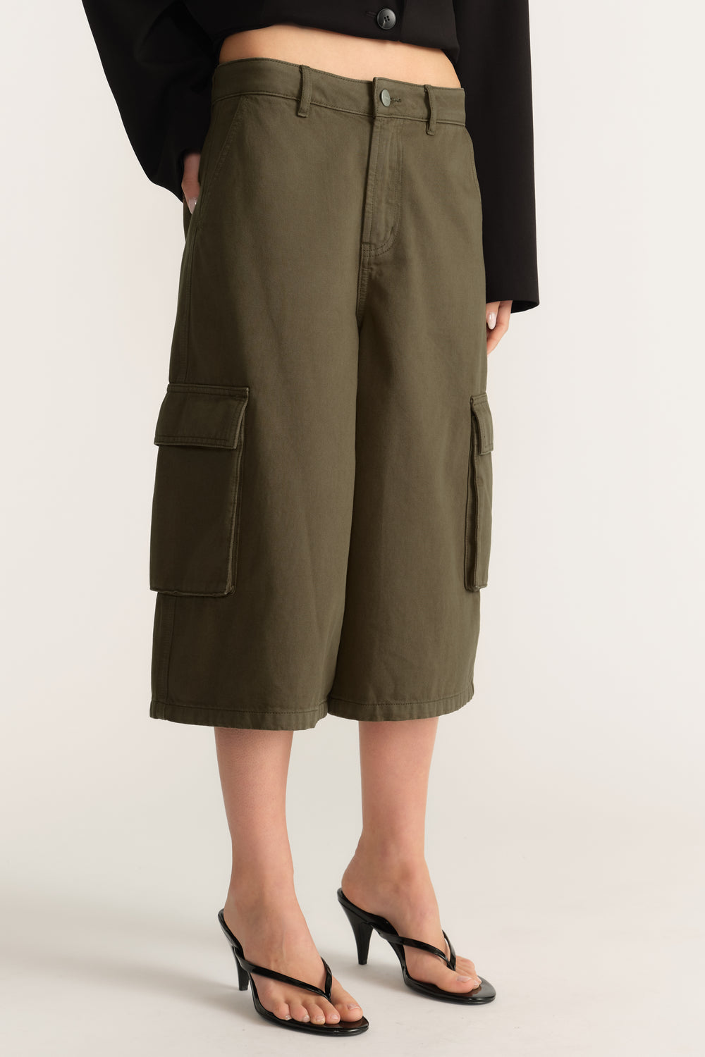 Woman wearing olive cargo shorts with a black cropped jacket and strappy heels