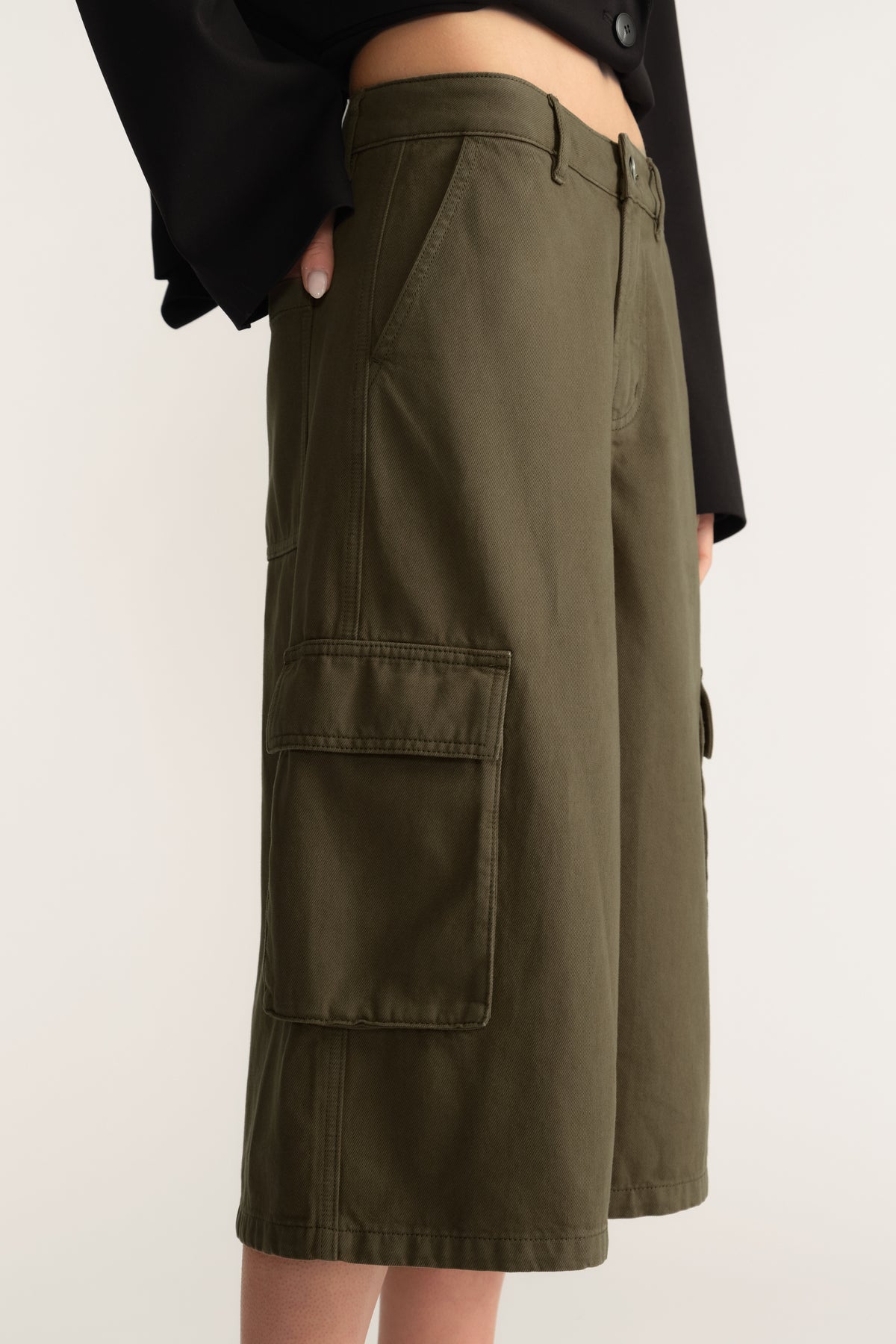 Woman wearing olive wide leg cargo shorts with utility pockets and a black cropped top