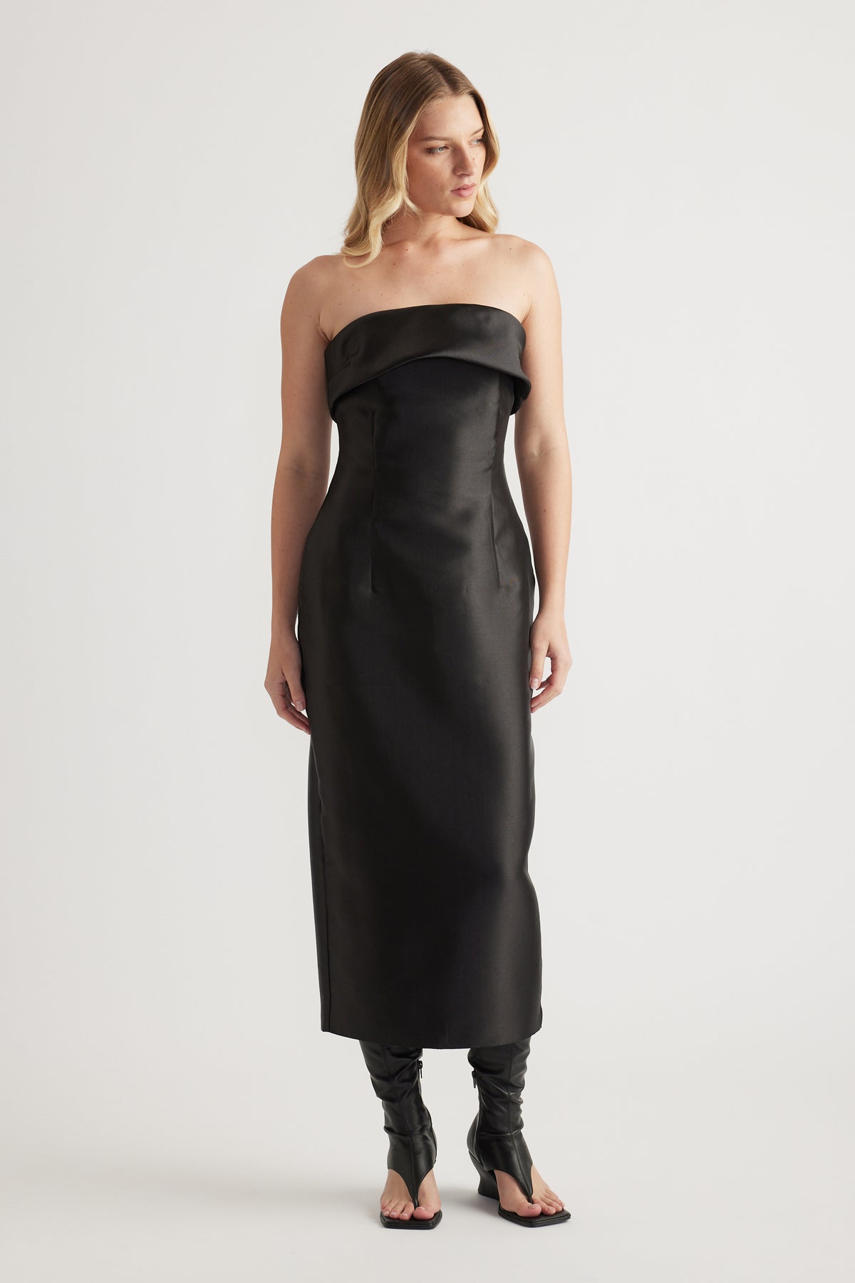 Woman wearing a black strapless fitted midi dress with a folded neckline and structured finish