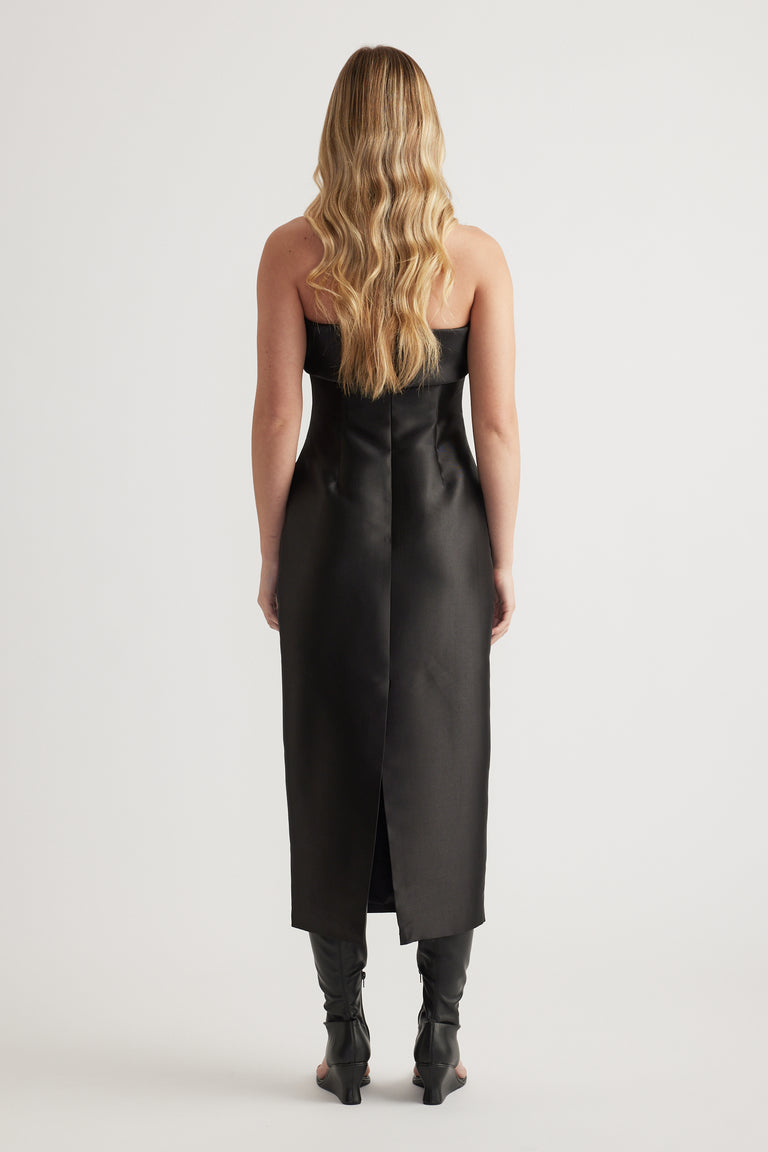 Woman wearing a fitted black midi dress with a straight neckline and ankle boots, viewed from behind