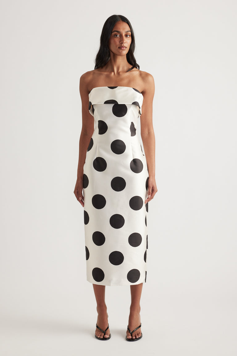 Woman wearing a strapless white midi dress with black polka dots and a fitted silhouette