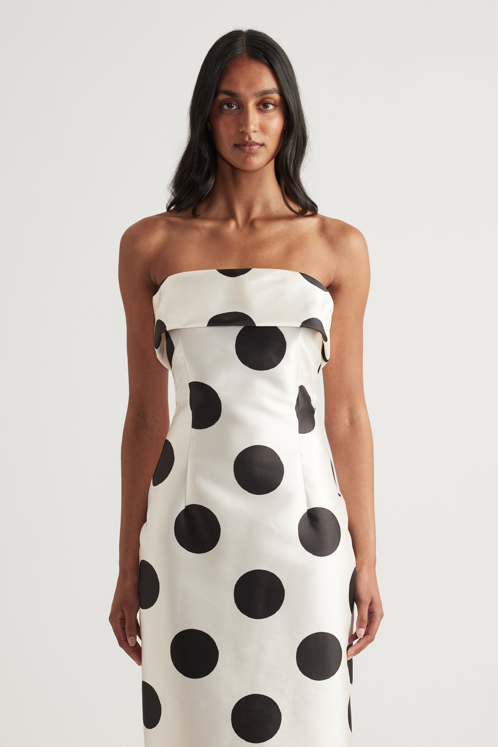 Woman wearing a white strapless midi dress with bold black polka dots and a fitted silhouette