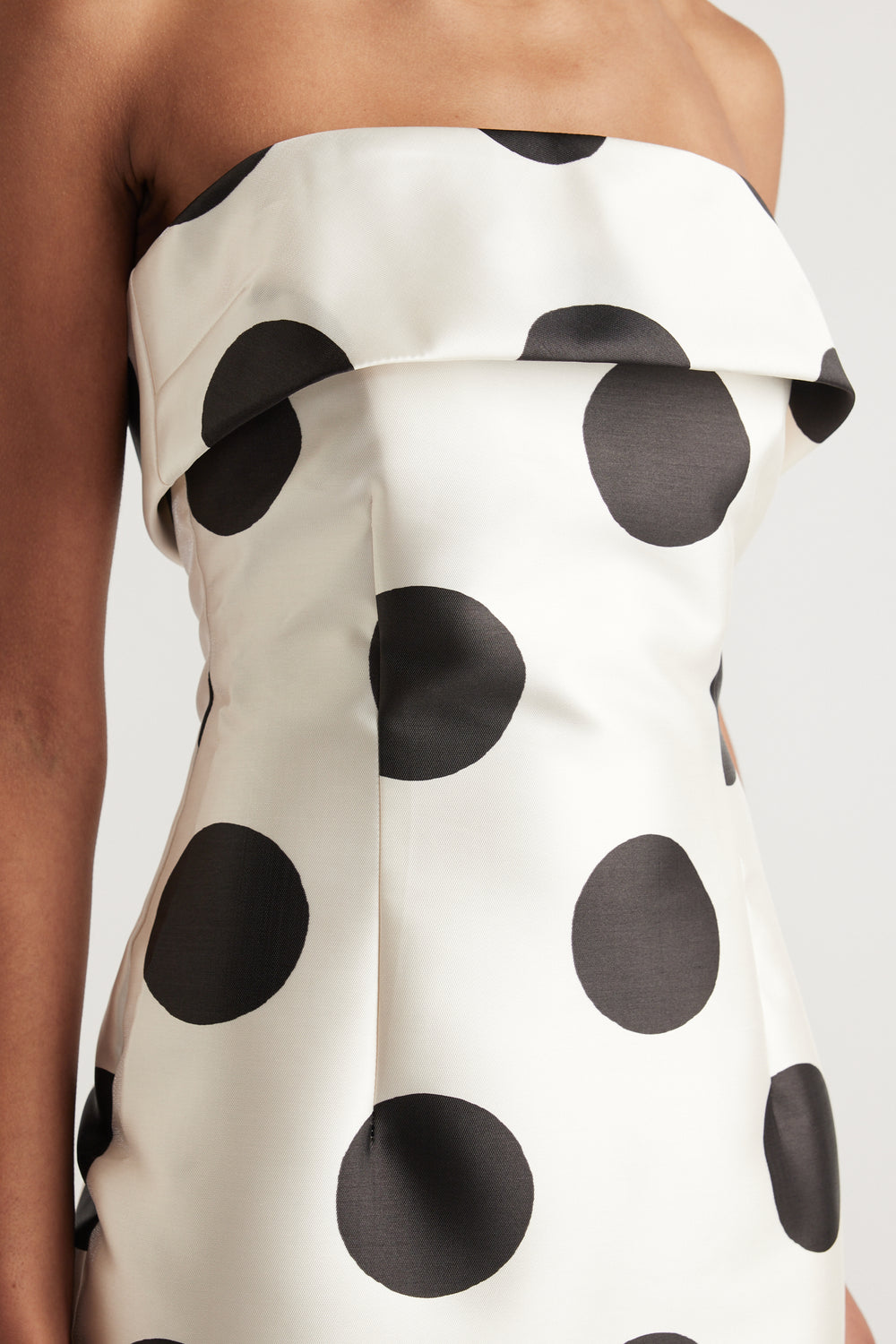 Woman wearing a white strapless midi dress with black polka dots and a fitted silhouette