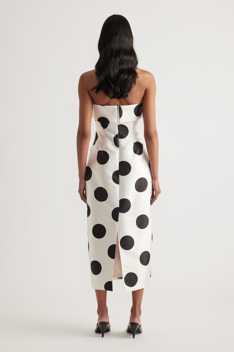 Woman wearing a strapless white midi dress with black polka dots and a back slit, viewed from behind