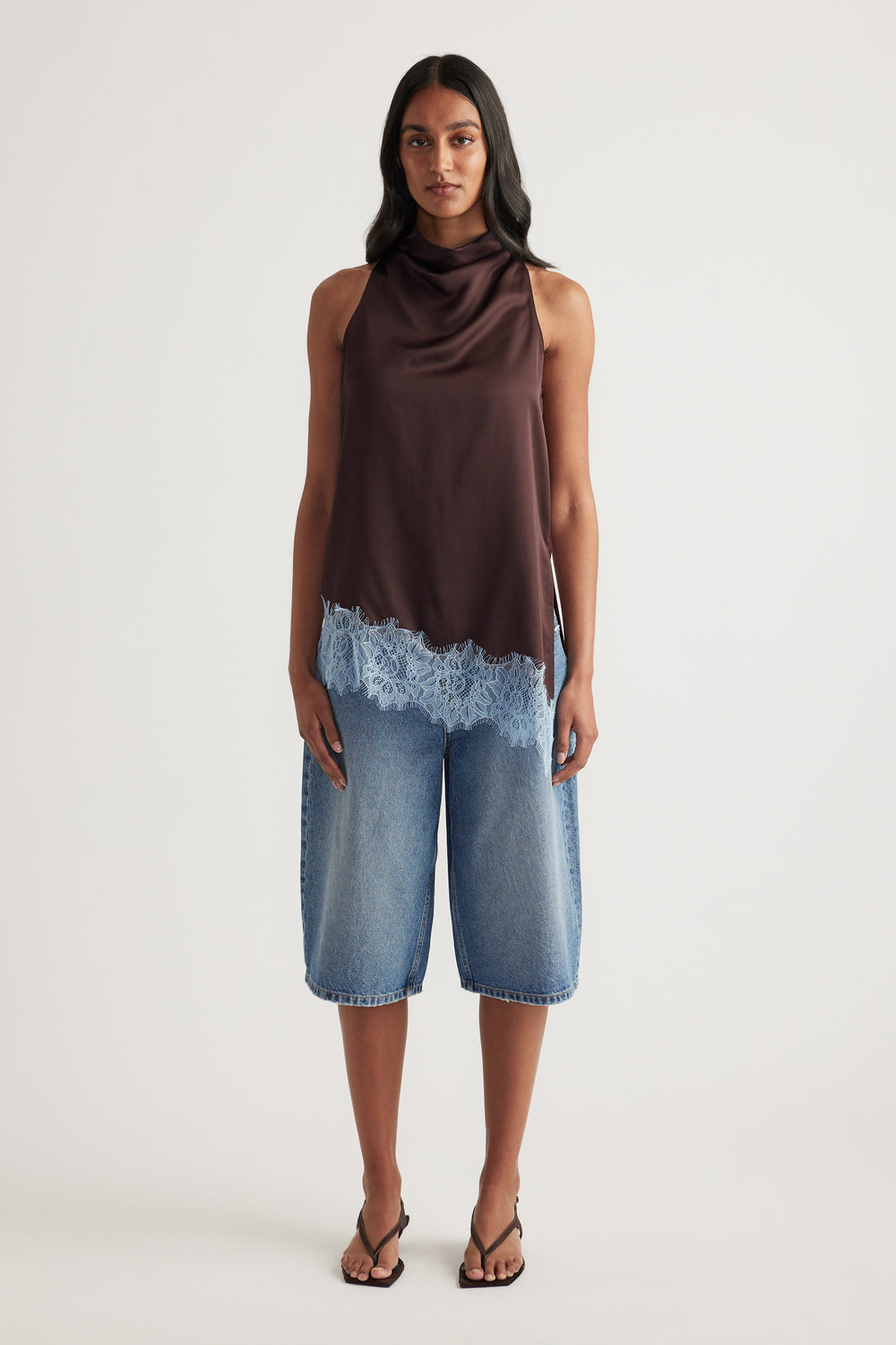 Woman wearing a chocolate brown sleeveless cowl neck top with lace trim and cropped blue wide leg jeans
