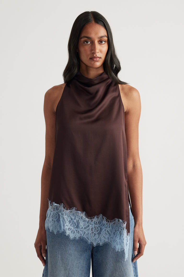 Woman wearing a chocolate brown sleeveless cowl neck top with blue lace trim and jeans