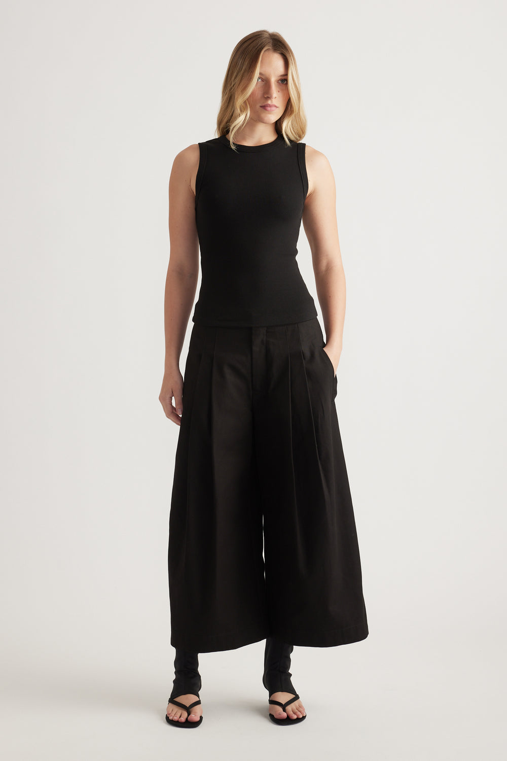 Woman wearing a black ribbed scoop neck tank with wide leg pants and flat sandals