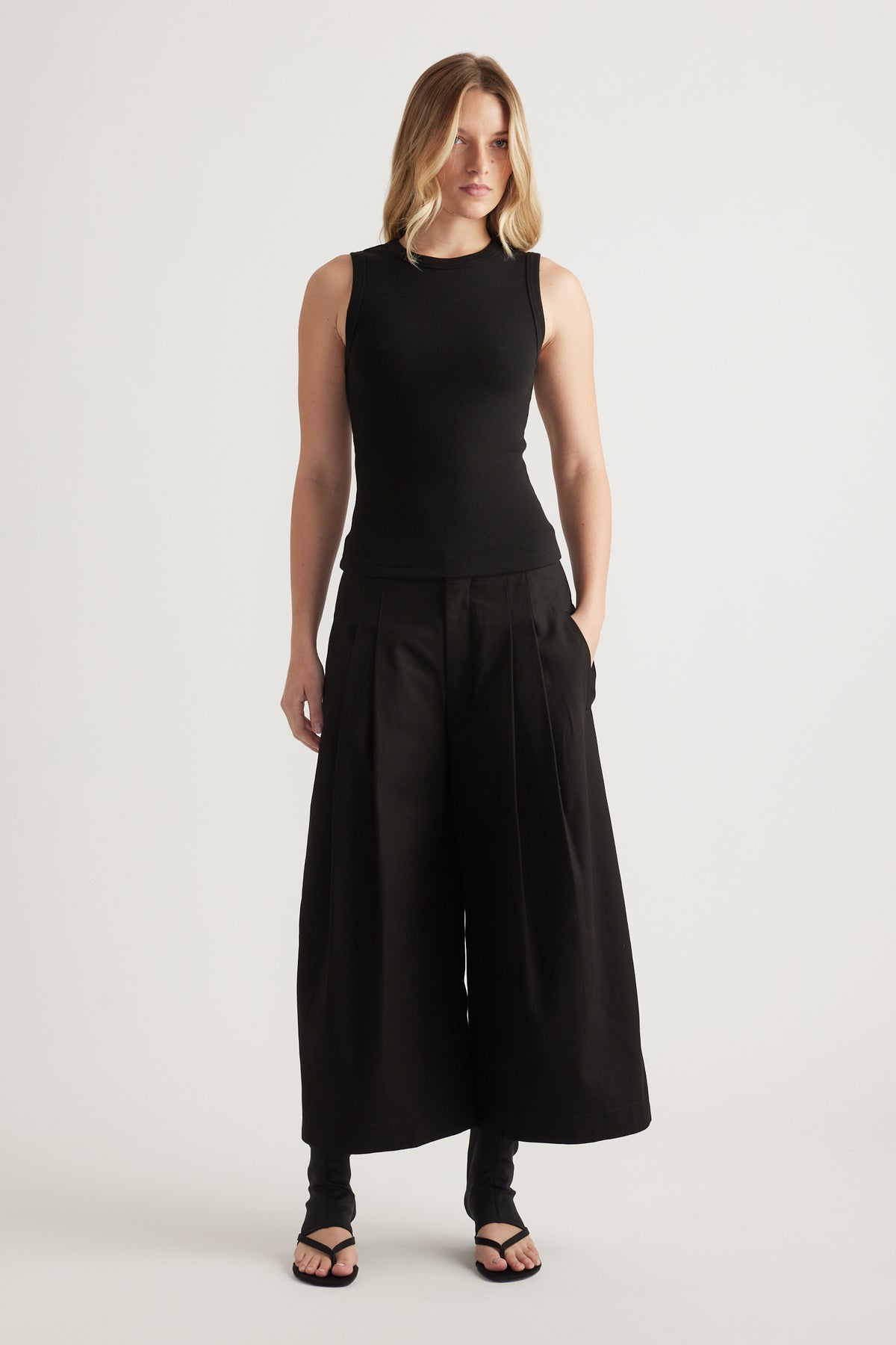 Woman wearing a black ribbed scoop neck tank with wide leg pants and flat sandals