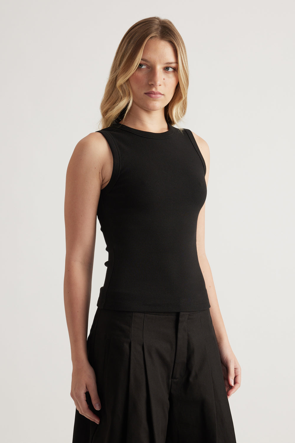 Woman wearing a black fitted ribbed tank with a scoop neck and black pleated pants