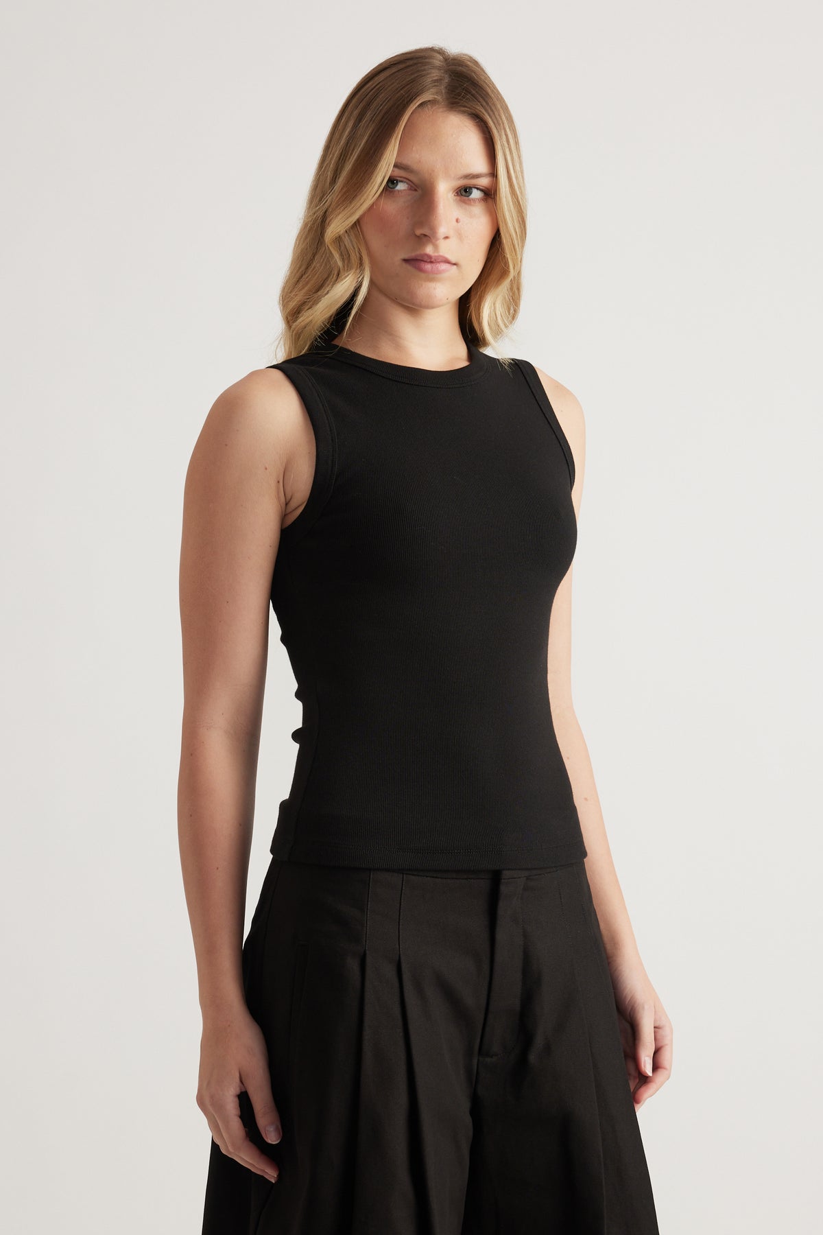 Woman wearing a black fitted ribbed tank with a scoop neck and black pleated pants