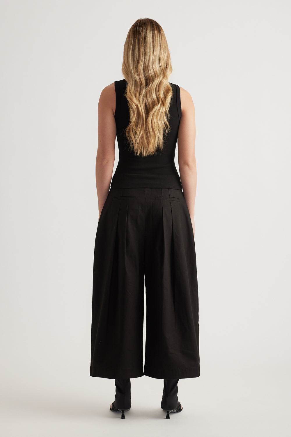Woman viewed from behind wearing a black sleeveless rib tank with black wide leg pants