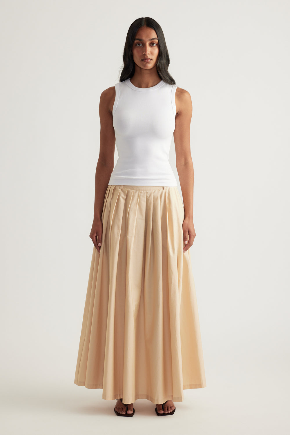 Woman wearing a fitted white ribbed tank with a scoop neckline and beige flowing maxi skirt