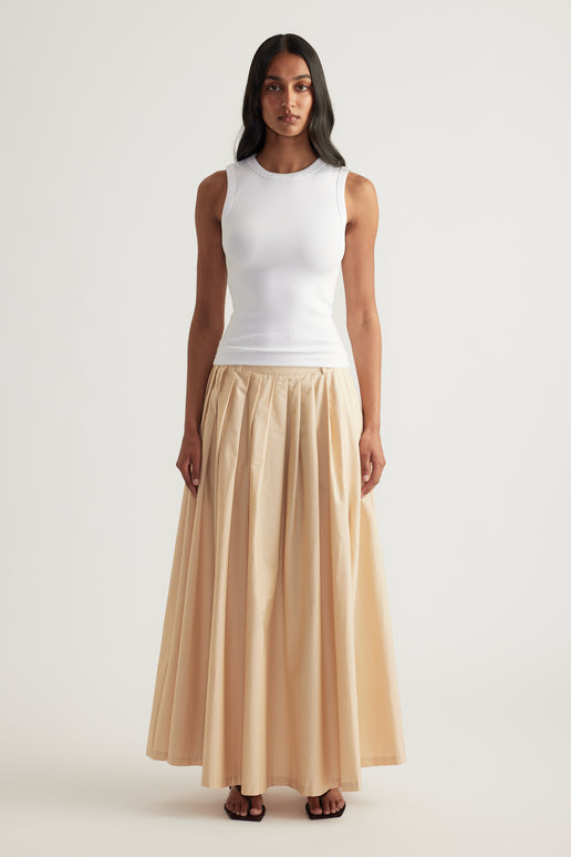 Woman wearing a fitted white ribbed tank with a scoop neckline and beige flowing maxi skirt