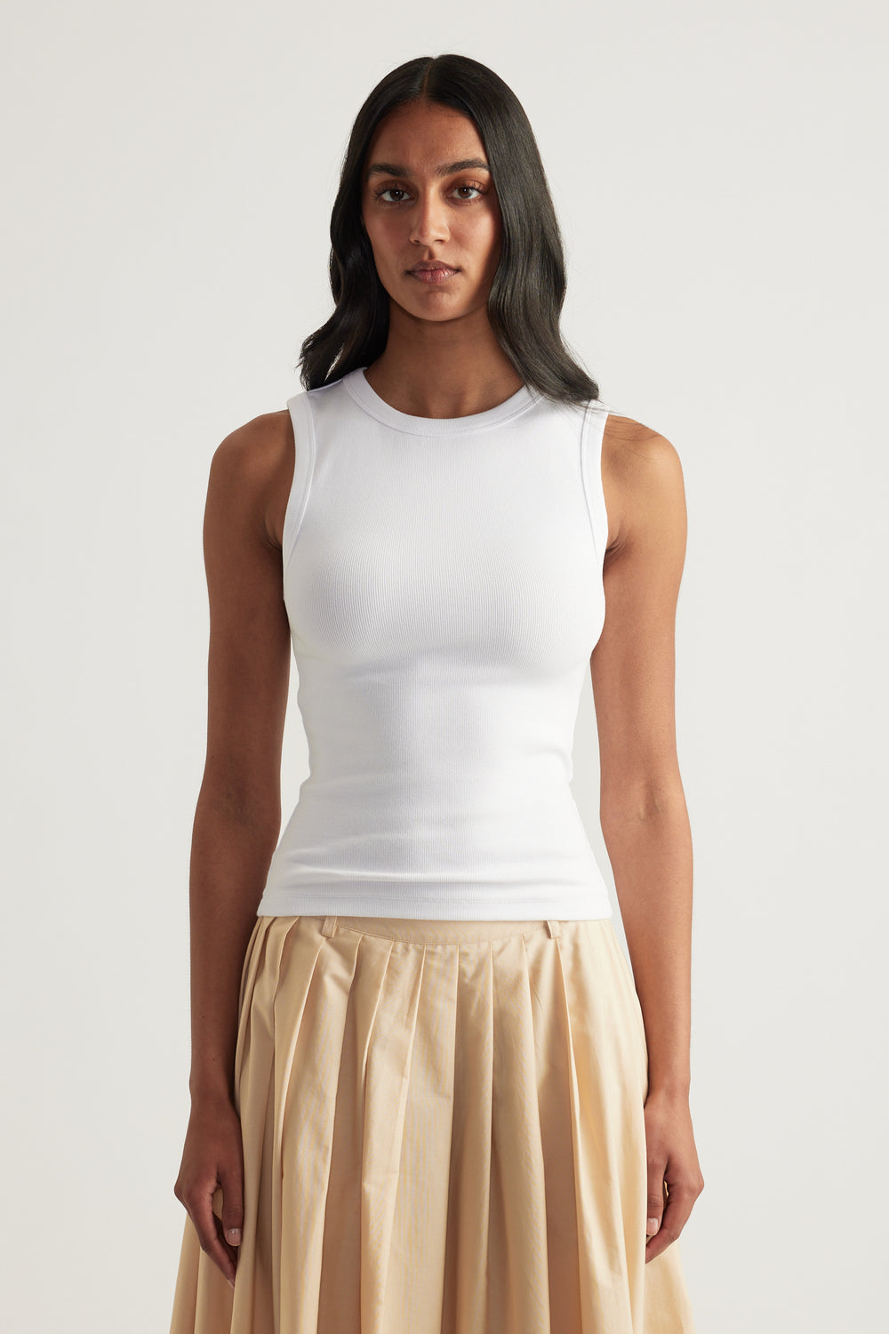 Woman wearing a fitted white ribbed tank top with a scoop neckline and sleeveless design