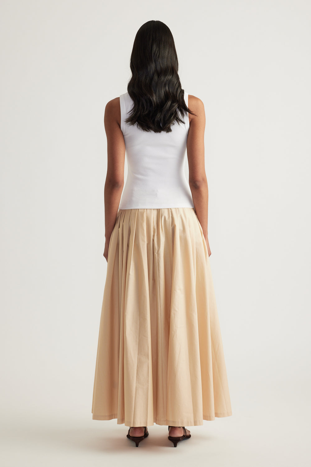 Woman viewed from behind wearing a white sleeveless rib tank and flowing beige maxi skirt