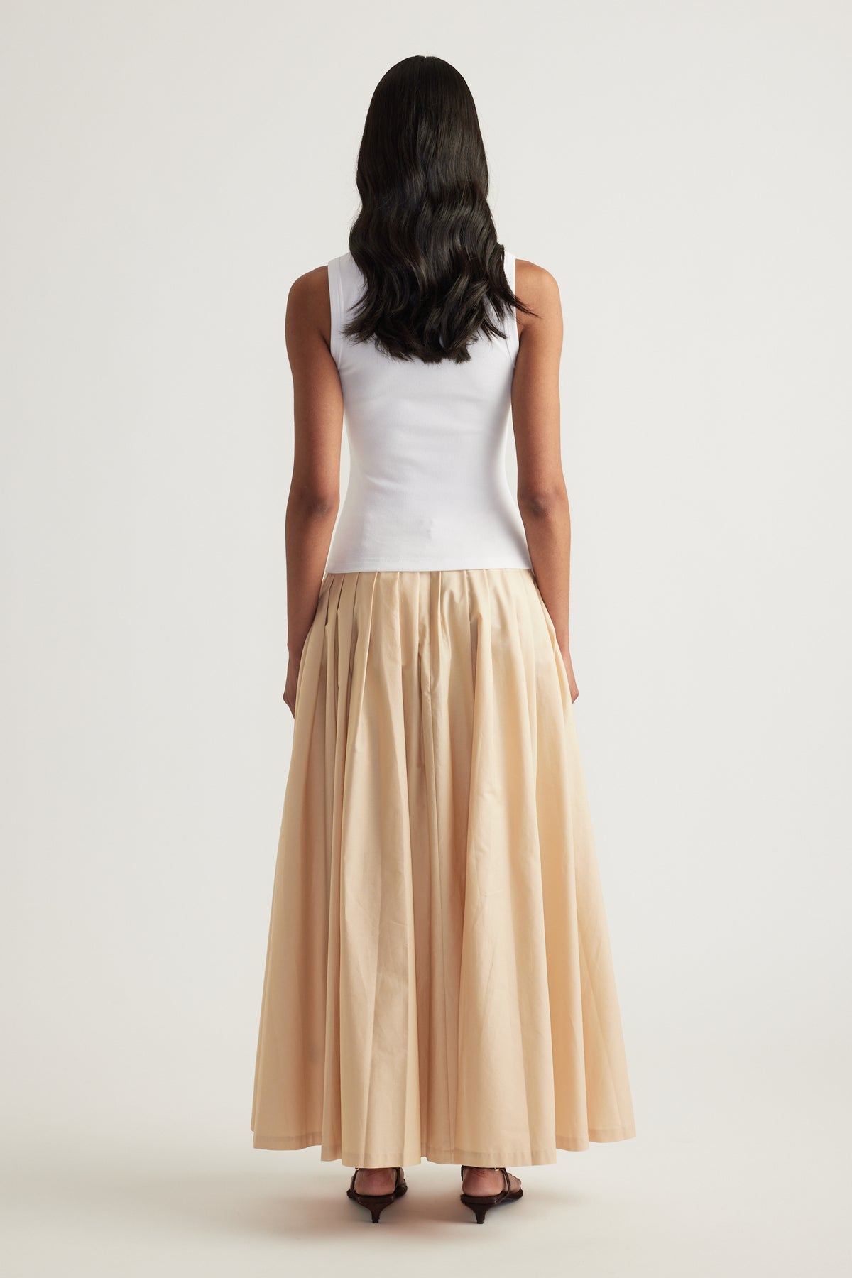 Woman viewed from behind wearing a white sleeveless rib tank and flowing beige maxi skirt
