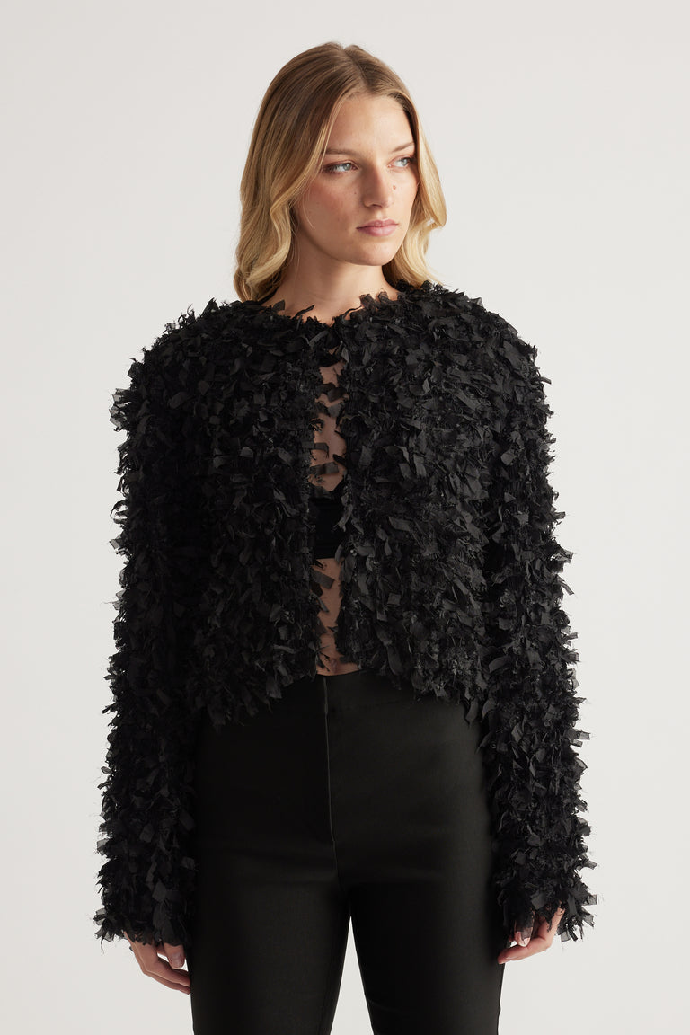 Model wearing a black textured jacket with long sleeves and a round neckline with black trousers