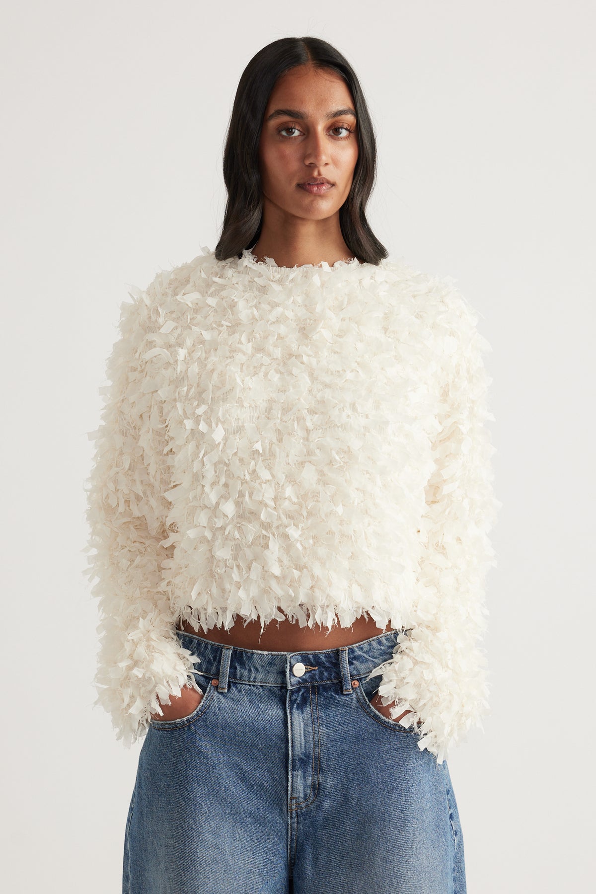 Woman wearing a cream textured cropped long sleeve top with blue high waisted jeans