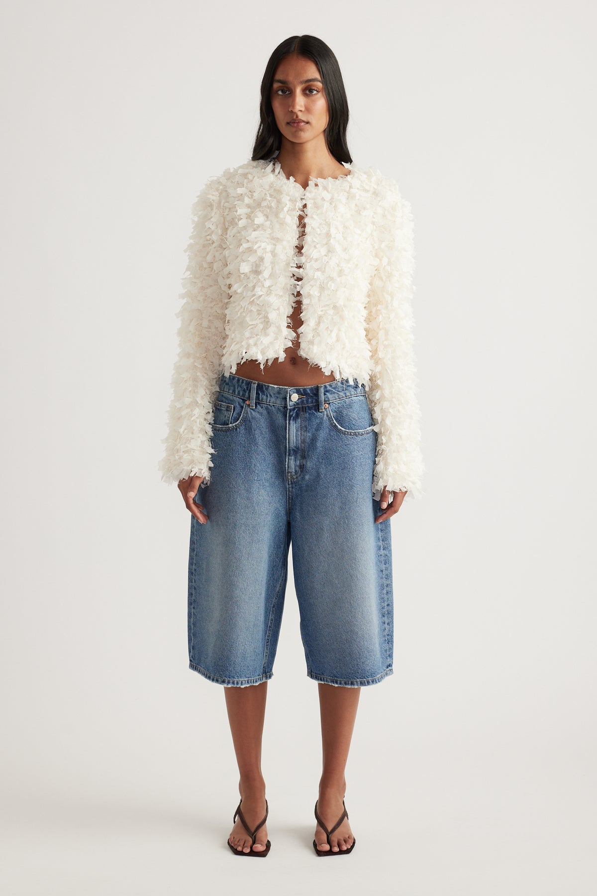 Woman wearing a cream textured jacket with blue denim knee-length shorts and strappy sandals