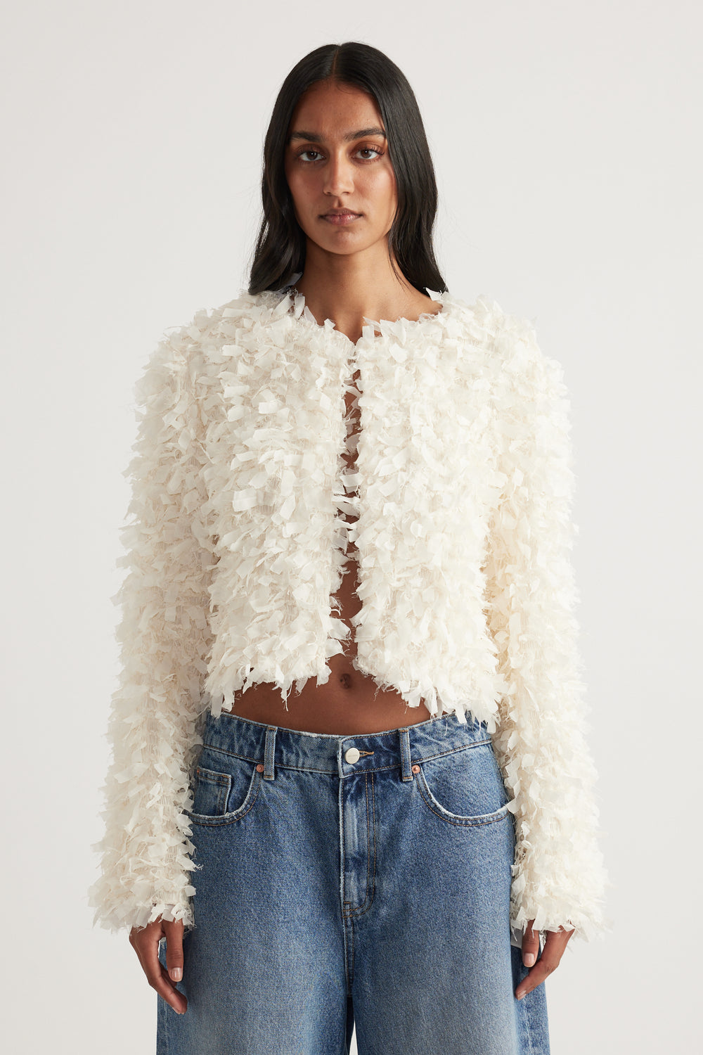 Woman wearing a cream textured jacket with long sleeves and blue jeans