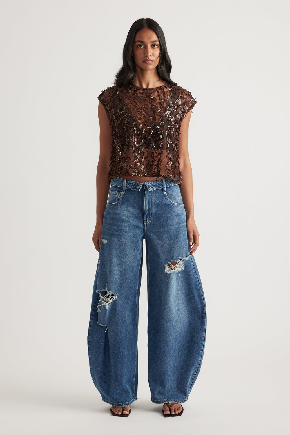 Woman wearing a sheer brown sequin crop top with wide leg distressed blue jeans