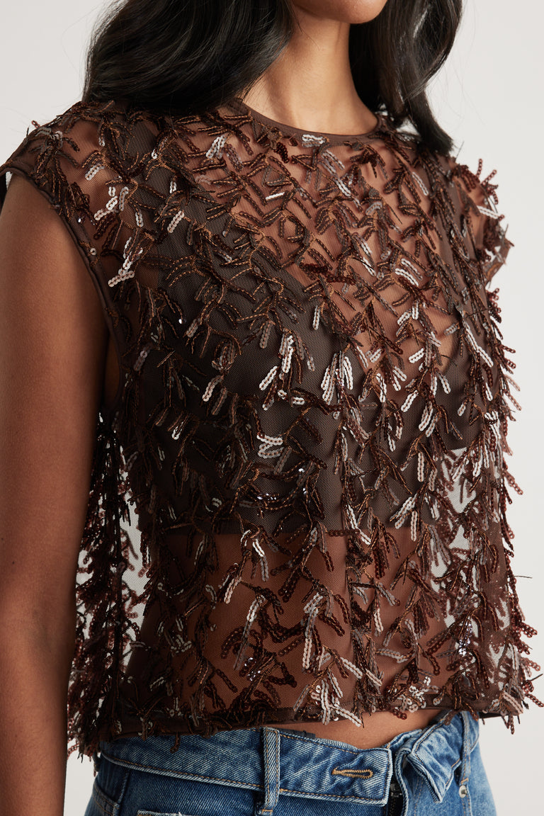 Woman wearing a sheer brown sequin cropped top with blue jeans