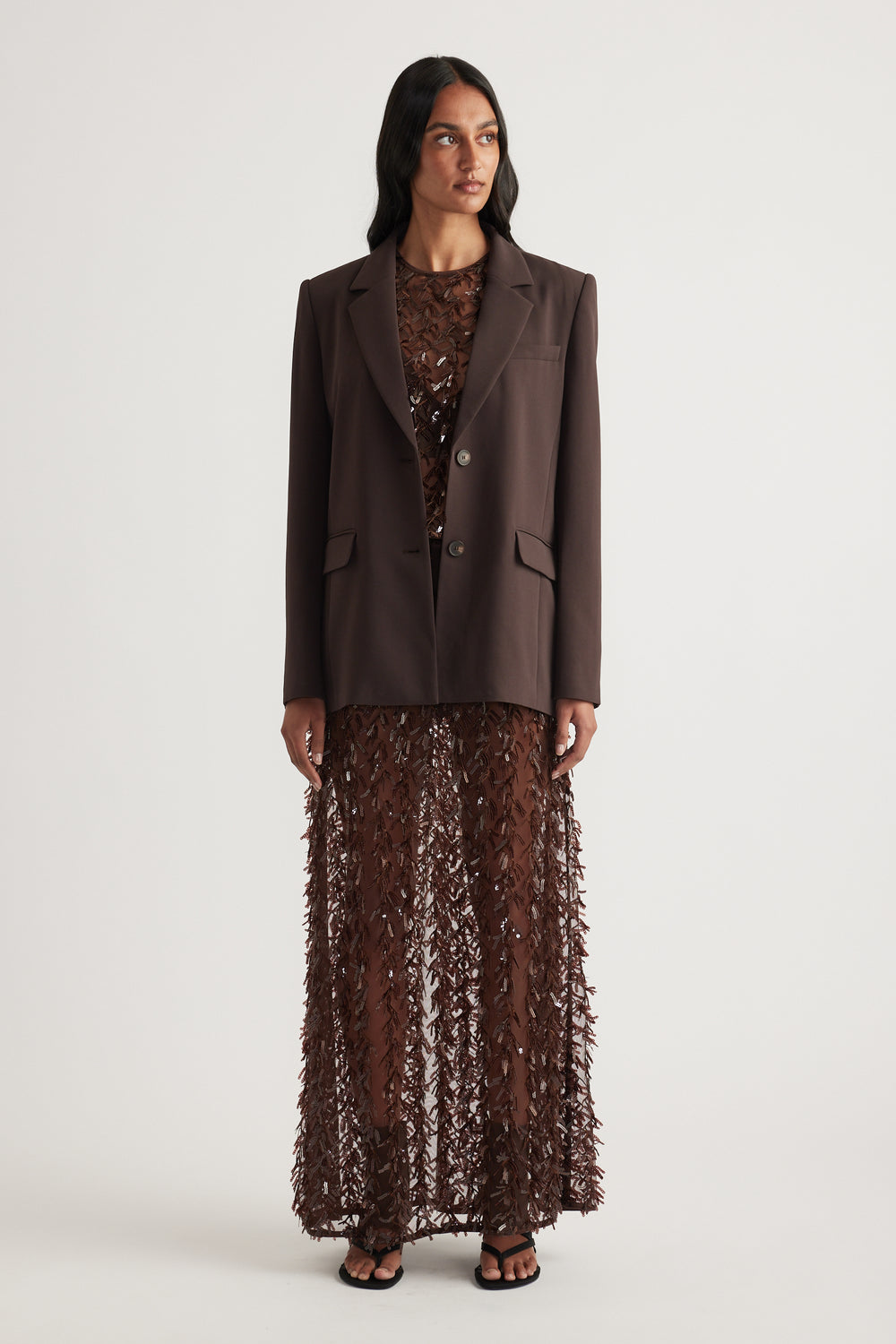 Woman wearing a brown tailored blazer with a sheer sequin maxi skirt and black sandals