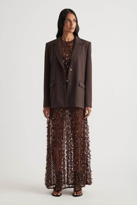 Woman wearing a brown tailored blazer with a sheer sequin maxi skirt and black sandals