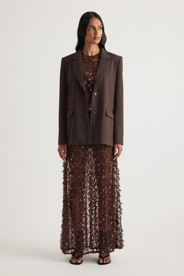 Woman wearing a brown tailored blazer with a sheer sequin maxi skirt and black sandals