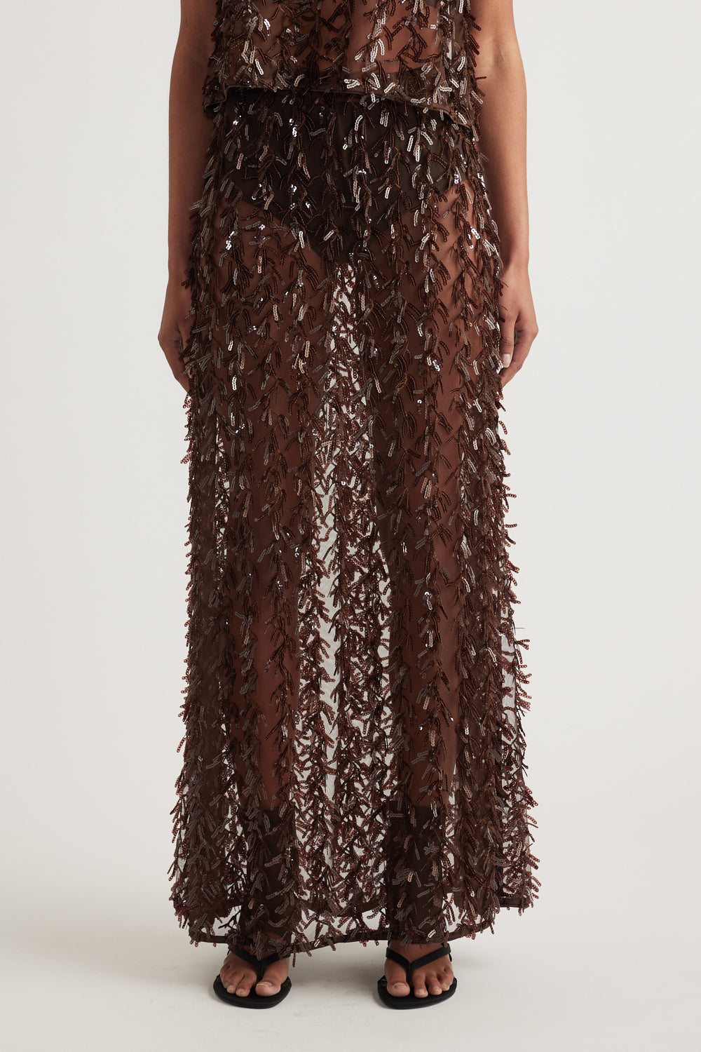 Woman wearing a brown sequin maxi skirt with sheer fringed texture and black sandals