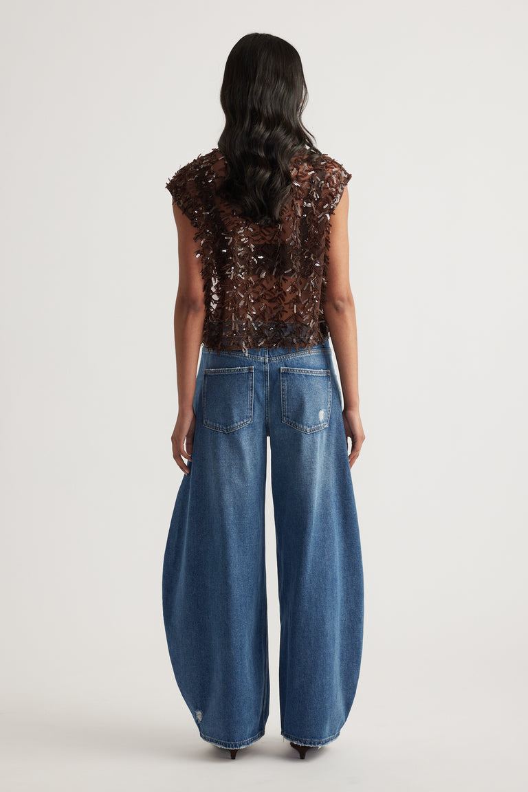 Woman seen from behind wearing a brown embellished sleeveless top and relaxed blue barrel leg jeans
