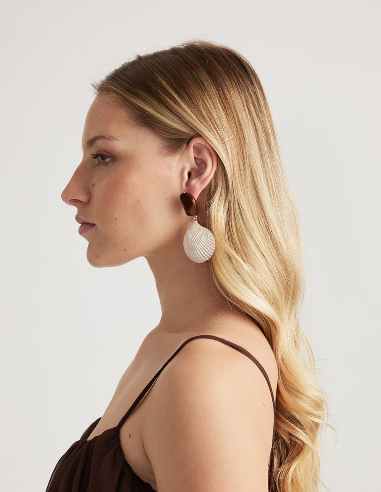 Woman wearing a large shell drop earring with a chocolate brown stone top