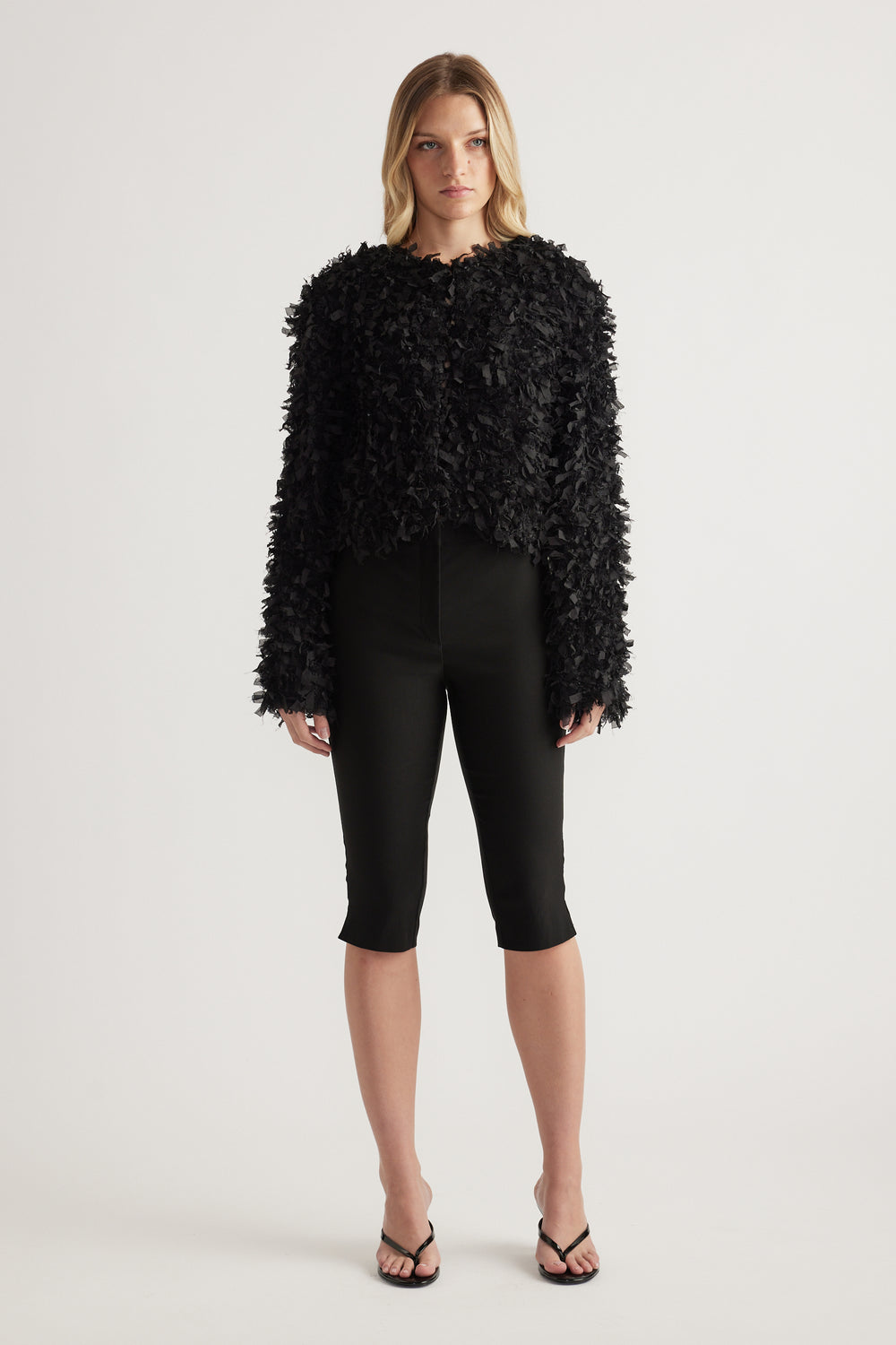 Woman wearing a black textured cropped jumper with slim black capri pants and strappy sandals