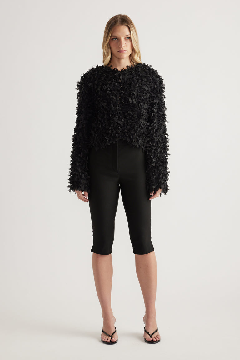 Woman wearing a black textured cropped jumper with slim black capri pants and strappy sandals