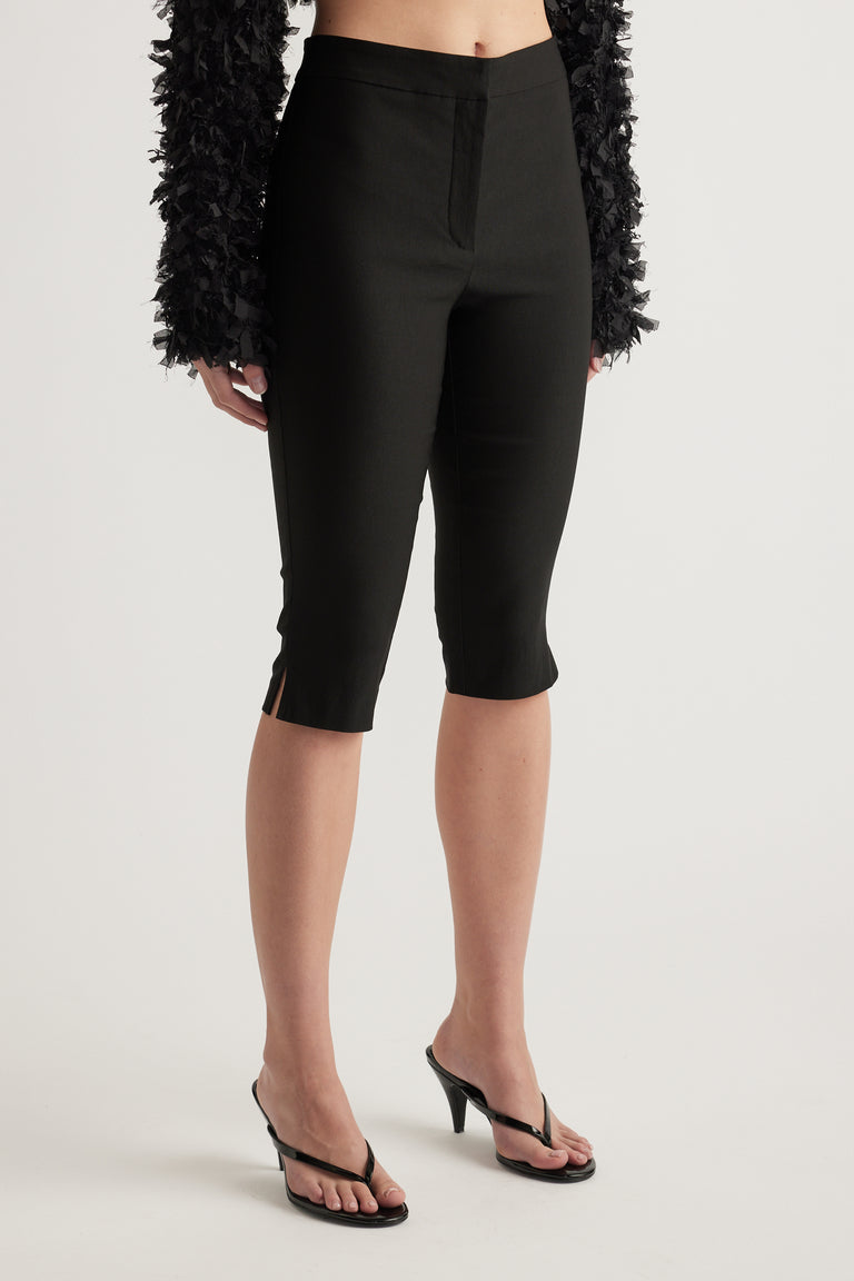 Woman wearing black slim fit capri pants with a mid rise waist and three quarter length hems